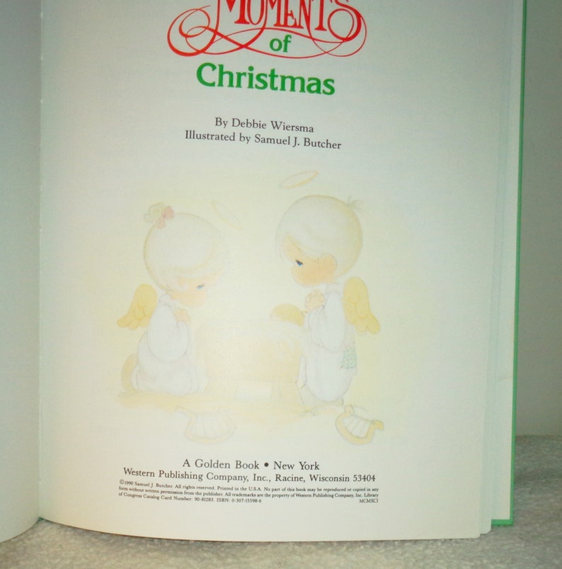May include: A book cover with a green border. The cover features two angels with halos, praying. The title of the book is "Moments of Christmas" by Debbie Wiersma, illustrated by Samuel J. Butcher. The book is published by Western Publishing Company, Inc.
