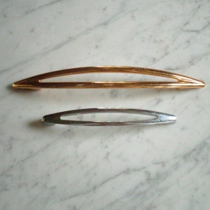 Op de afbeelding: Twee kastdeurgrepen, een gouden en een zilveren, op een witte marmeren achtergrond.