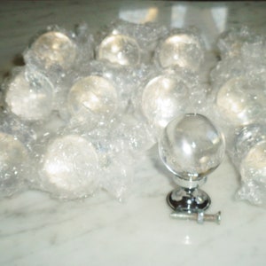 May include: A group of clear glass cabinet knobs with a chrome finish, packaged in bubble wrap. One knob is shown outside of the packaging with a screw.