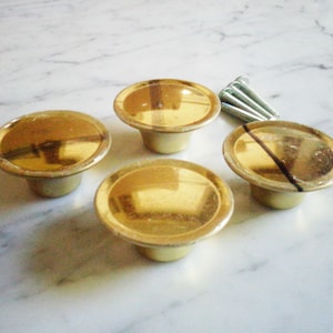 Op de afbeelding: Vier gouden kastknoppen met een afgeronde, licht gewelfde bovenkant. De knoppen zijn in een halve cirkel op een wit marmeren oppervlak gerangschikt.