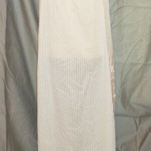 Puede incluir: Un vestido blanco de slip sin mangas, de canal&eacute;, con un ribete de encaje en el dobladillo. El vestido est&aacute; en un maniqu&iacute; blanco.