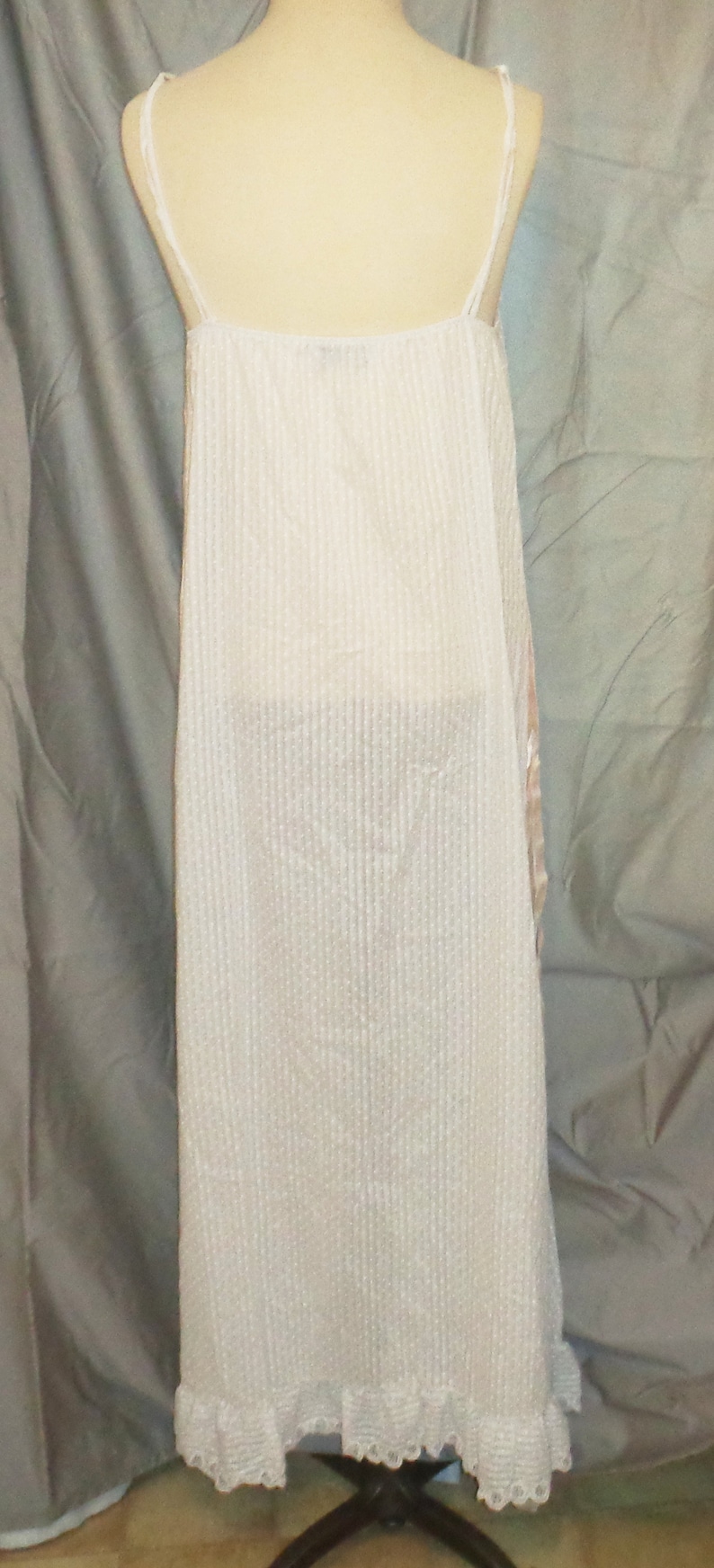 Puede incluir: Un vestido blanco de slip sin mangas, de canal&eacute;, con un ribete de encaje en el dobladillo. El vestido est&aacute; en un maniqu&iacute; blanco.