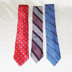 May include: Three neckties with different patterns. One is red with white polka dots, one is grey with burgundy and black stripes, and one is blue with white stripes.