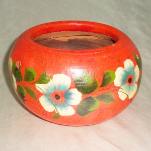 May include: A small, orange terracotta pot with hand-painted white and blue flowers and green leaves.