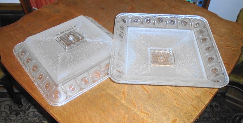 May include: Two clear glass serving dishes with a raised, embossed design. The dishes are square and have a frosted finish.