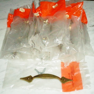 Puede incluir: Un paquete de tiradores de puerta de armario de latón con un solo tirador en una bolsa separada. Los tiradores están en bolsas de plástico individuales con un embalaje naranja. Los tiradores tienen un diseño simple y elegante.