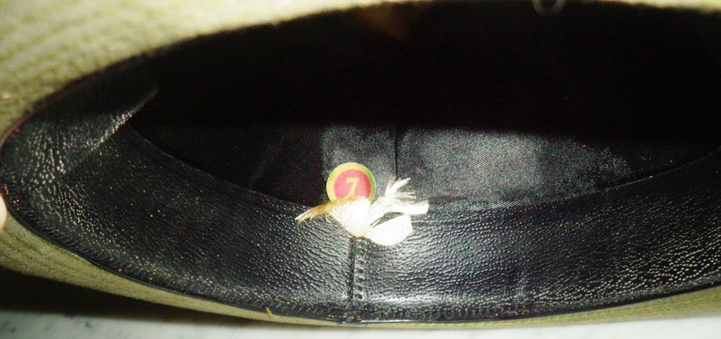 May include: The inside of a green felt hat with a black leather band. A small white tag with the number "7" is visible inside the hat.
