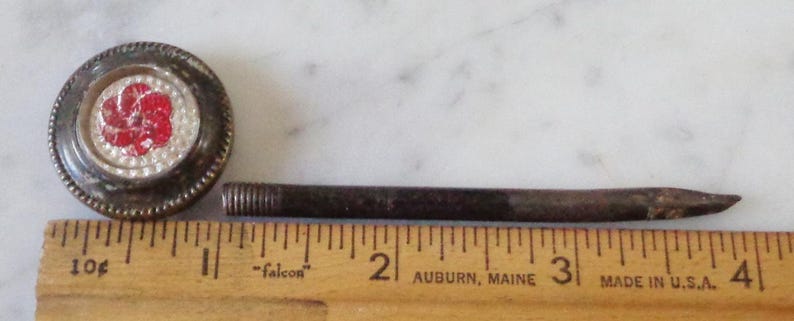 May include: A vintage metal knob with a red and white flower design and a matching metal rod. The rod is about 3 inches long.