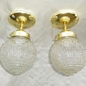 May include: Two gold ceiling light fixtures with clear glass globe shades. The shades have a diamond pattern.
