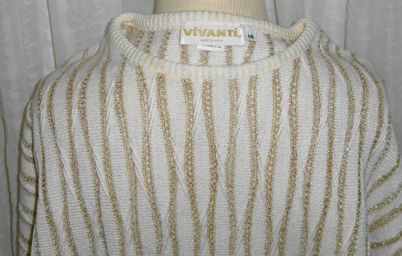 May include: White sweater with gold stripes. The sweater has a crew neck and is made of a soft, knit fabric. The label reads "VIVANTL. Made in U.S.A."