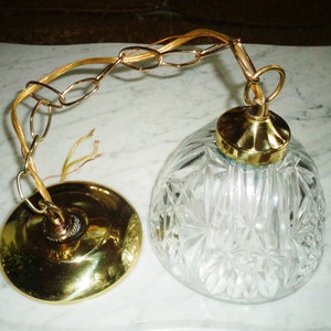 May include: A brass ceiling light fixture with a clear glass shade. The shade has a diamond pattern and is attached to a chain.