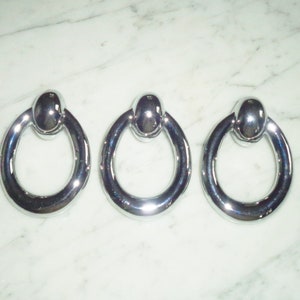 May include: Three silver ring-shaped door knobs with a round ball on top.