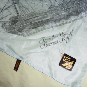 May include: A light blue silk scarf featuring a detailed black and white illustration of a sailing ship. The scarf has the text "From the House of Borkum Riff" and a tag that reads "B.N."
