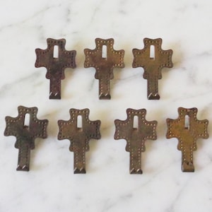 Könnte beinhalten: Acht antike Messinghaken in Kreuzform. Die Haken sind verziert mit einer strukturierten Oberfläche und einem kleinen Loch in der Mitte.