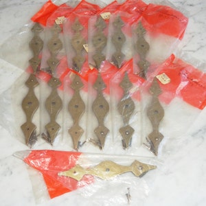 Puede incluir: Un paquete de 12 tiradores de cajón de metal dorado con un diseño geométrico. Los tiradores están empaquetados en bolsas de plástico transparentes con etiquetas rojas.