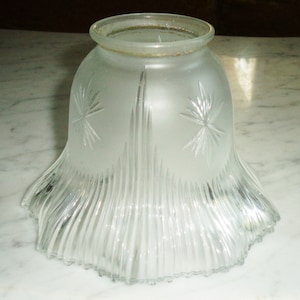 May include: A bell-shaped glass lamp shade featuring a frosted finish on the upper section with etched starburst patterns. The lower portion is made of clear glass with vertical fluted ribbing that extends to the scalloped, ruffled bottom edge.