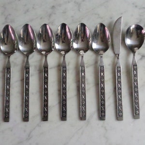 May include: Set of eight silver-toned spoons and a knife with decorative floral patterns on the handles.
