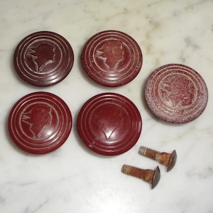 May include: Five red plastic buttons with a raised profile and a silhouette of a woman's head in the center. The buttons have a concentric circle design around the silhouette. Two screws are also visible in the image.