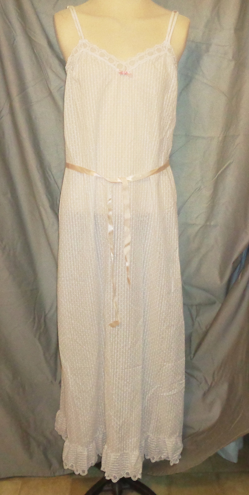 Puede incluir: Un vestido blanco de algod&oacute;n con ribete de encaje y un lazo de cinta de sat&eacute;n. El vestido tiene un corpi&ntilde;o ajustado y una falda fluida.