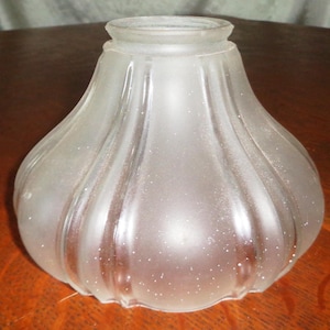 May include: A frosted glass lampshade with a bulbous shape and vertical ribbed detailing. The shade has a slightly flared top and a rounded bottom. The glass has a subtle sparkle, adding a touch of elegance to the design.