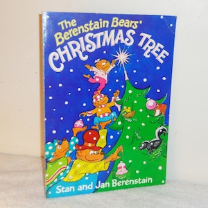 May include: A vintage children's book cover featuring the Berenstain Bears decorating a Christmas tree. The cover is blue with white snowflakes and the title "The Berenstain Bears' Christmas Tree" in yellow, red, and green letters. The book is by Stan and Jan Berenstain.