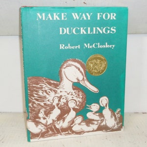 May include: A teal blue book cover with the title "Make Way for Ducklings" by Robert McCloskey. The cover features an illustration of a mother duck and her ducklings.