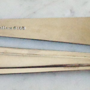 May include: Two silver spoons with a simple design. The spoon on top has the inscription "&copy;Talien Silver" on the back.