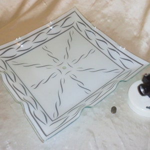 May include: A white glass ceiling light fixture with a silver decorative border and a starburst design. The fixture is attached to a white ceiling mount with a black electrical box.