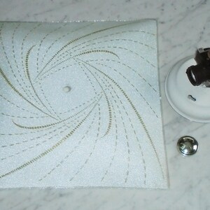 Pode incluir: Lumin&aacute;ria de teto branca com um padr&atilde;o de espiral em dourado e branco. A lumin&aacute;ria tem uma cobertura de pl&aacute;stico branco e uma base de metal.