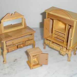 May include: Three wooden dollhouse furniture pieces: a vanity with a mirror and drawers, a tall cabinet with a door and drawers, and a small cabinet with a door. All pieces are made of unfinished wood.