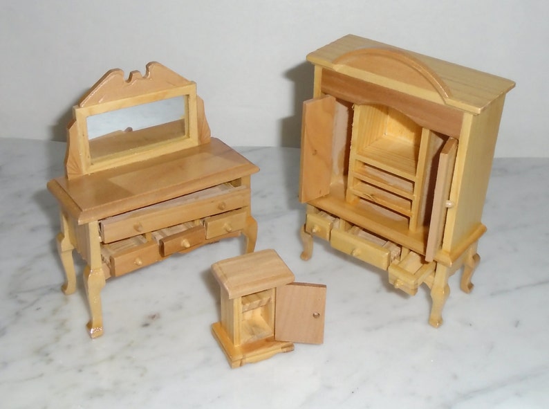 May include: Three wooden dollhouse furniture pieces: a vanity with a mirror and drawers, a tall cabinet with a door and drawers, and a small cabinet with a door. All pieces are made of unfinished wood.