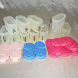 May include: A set of clear plastic spice containers with black labels. The labels include "Garlic Salt", "Celery Seed", "Minced Onion", "Parsley", "Oregano", "Poultry Seasoning", "Paprika", "Seasoning Salt", and "Garlic Powder". There are also pink and blue spice containers with lids.