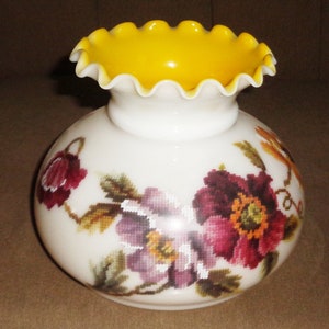 Könnte beinhalten: Weißer Lampenschirm aus Glas mit einem gelben, gekräuselten Oberteil und einem Blumendesign mit violetten, roten und grünen Blumen.