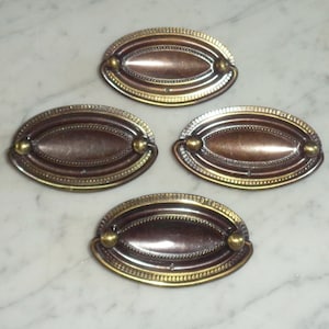 May include: Four oval-shaped cabinet pulls with a brass finish and a copper centre. The pulls have a decorative border and two round knobs.