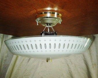 Może przedstawiać: Biała lampa sufitowa z kloszem z matowego szkła, na którym widoczny jest geometryczny wzór z kół i gwiazd. Lampa ma chromowane wykończenie i prosty design.