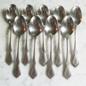 May include: A set of ten silver teaspoons with ornate handles. The spoons are arranged in a row, with the handles pointing upwards.