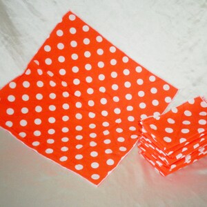 Pu&ograve; includere: Tovaglioli arancioni brillanti con pois bianchi. L'immagine mostra una pila di tovaglioli piegati e due tovaglioli aperti. I tovaglioli sono realizzati in un materiale morbido e sono adatti per una festa o un evento.