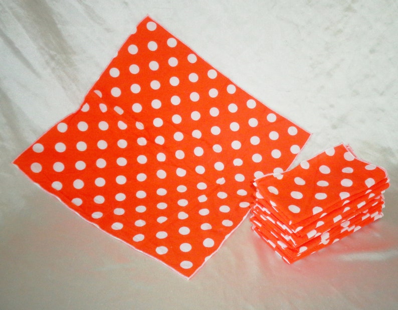 Pu&ograve; includere: Tovaglioli arancioni brillanti con pois bianchi. L'immagine mostra una pila di tovaglioli piegati e due tovaglioli aperti. I tovaglioli sono realizzati in un materiale morbido e sono adatti per una festa o un evento.
