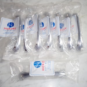 Puede incluir: Diez tiradores de puerta de armario plateados envasados individualmente en bolsas de plástico transparentes. Cada bolsa tiene una etiqueta blanca con el texto "Hickory Hardware" y un logotipo de un árbol estilizado.