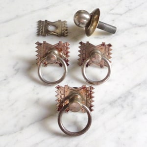 May include: Three antique silver-toned cabinet knobs with a ring pull and a square base with a decorative design. One knob has a round ball finial.