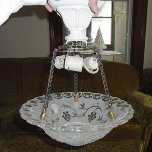 May include: A white ceiling fixture with a frosted glass bowl shade featuring a grapevine design. The shade is suspended by three chains and has a scalloped edge.
