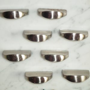 Peut inclure: Huit boutons de cabinet en argent de forme arrondie en demi-cercle. Les boutons sont disposés en deux rangées de quatre sur une surface en marbre blanc.
