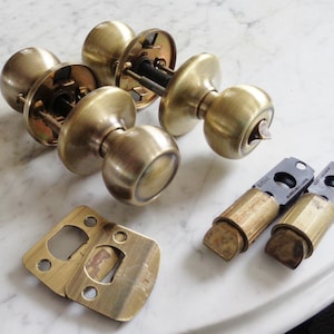 Puede incluir: Un juego de dos pomos de puerta de latón con una cerradura y un pestillo. Los pomos tienen un acabado en latón pulido. El juego también incluye dos llaves de latón y una placa de golpe de latón.