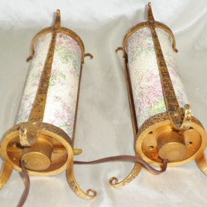 May include: Two gold-toned metal table lamps with a floral patterned glass shade. The lamps have a round base with three legs.
