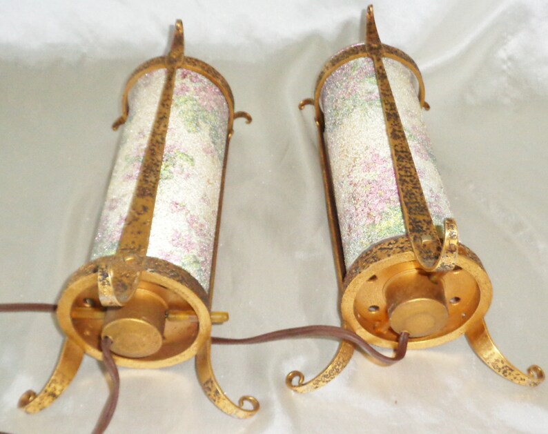 May include: Two gold-toned metal table lamps with a floral patterned glass shade. The lamps have a round base with three legs.