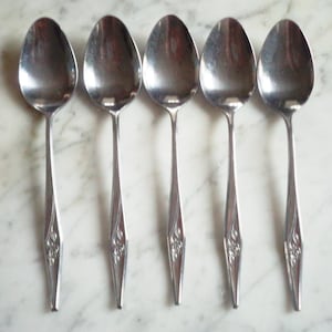 May include: Five silver spoons with ornate handles. The spoons have a rounded bowl and a long, slender handle with a decorative design.