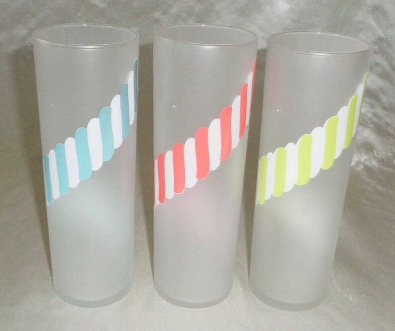 May include: Three frosted glass tumblers with a diagonal stripe design. The tumblers have a white background with blue, pink, and yellow stripes.