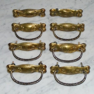 Puede incluir: Ocho tiradores de cajón de latón antiguo con detalles ornamentados. Cada tirador tiene una manija curva y una placa rectangular con un centro elevado. Los tiradores están en buen estado con algunos signos de edad y desgaste.