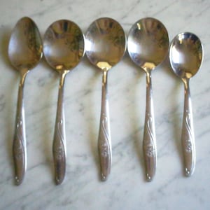 Könnte beinhalten: Satz von fünf silbernen Löffeln mit verzierten Blumendesigns auf den Griffen.