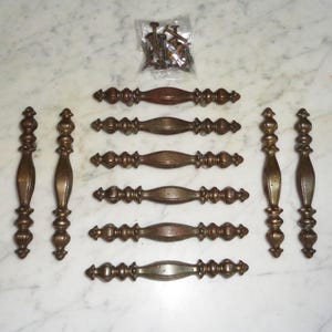 May include: Set of eight antique brass cabinet pulls with ornate details. The pulls are in various sizes and shapes, with some featuring a rounded top and others a more rectangular shape. The pulls are all in good condition with a warm, aged patina.